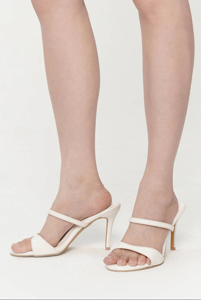 White high-heeled sandals worn with sheer stockings on a white background