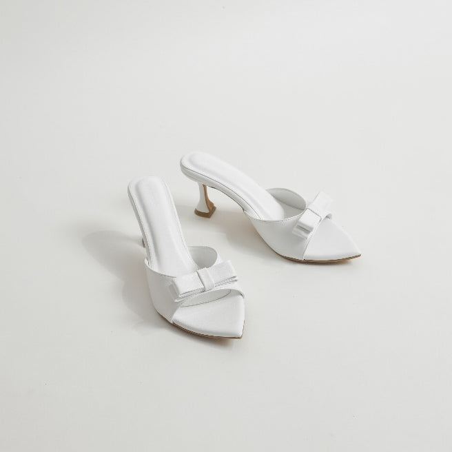 Pair of white high-heeled shoes with bow details on a light gray background