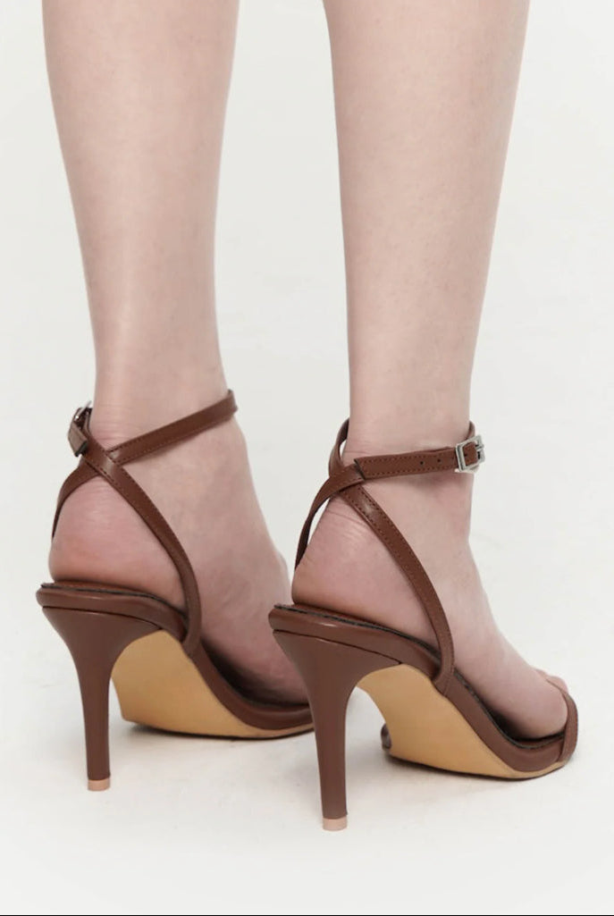 Brown high-heeled sandals worn with sheer stockings on a  background