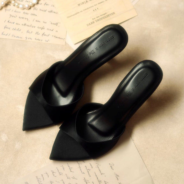 Black pointed-toe shoes on a textured surface with handwritten text.