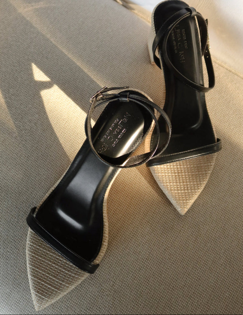 Black high-heeled shoes with a unique design on a textured beige surface