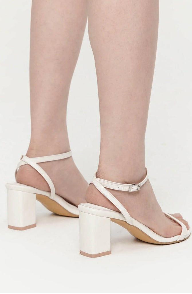 White high-heeled sandals worn with sheer tights on a white background