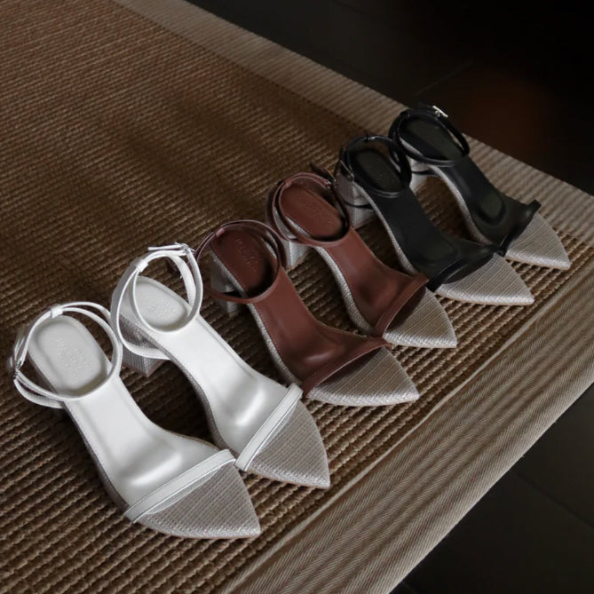 Set of four high-heeled shoes in white, brown, and black on a textured surface.