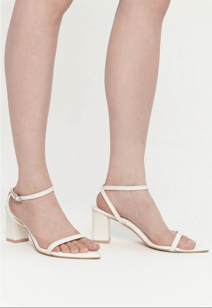 White sandals with block heels worn by a person on a white background