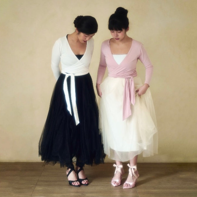 Two women wearing matching outfits with black and white, and pink and white dresses against a beige background.
