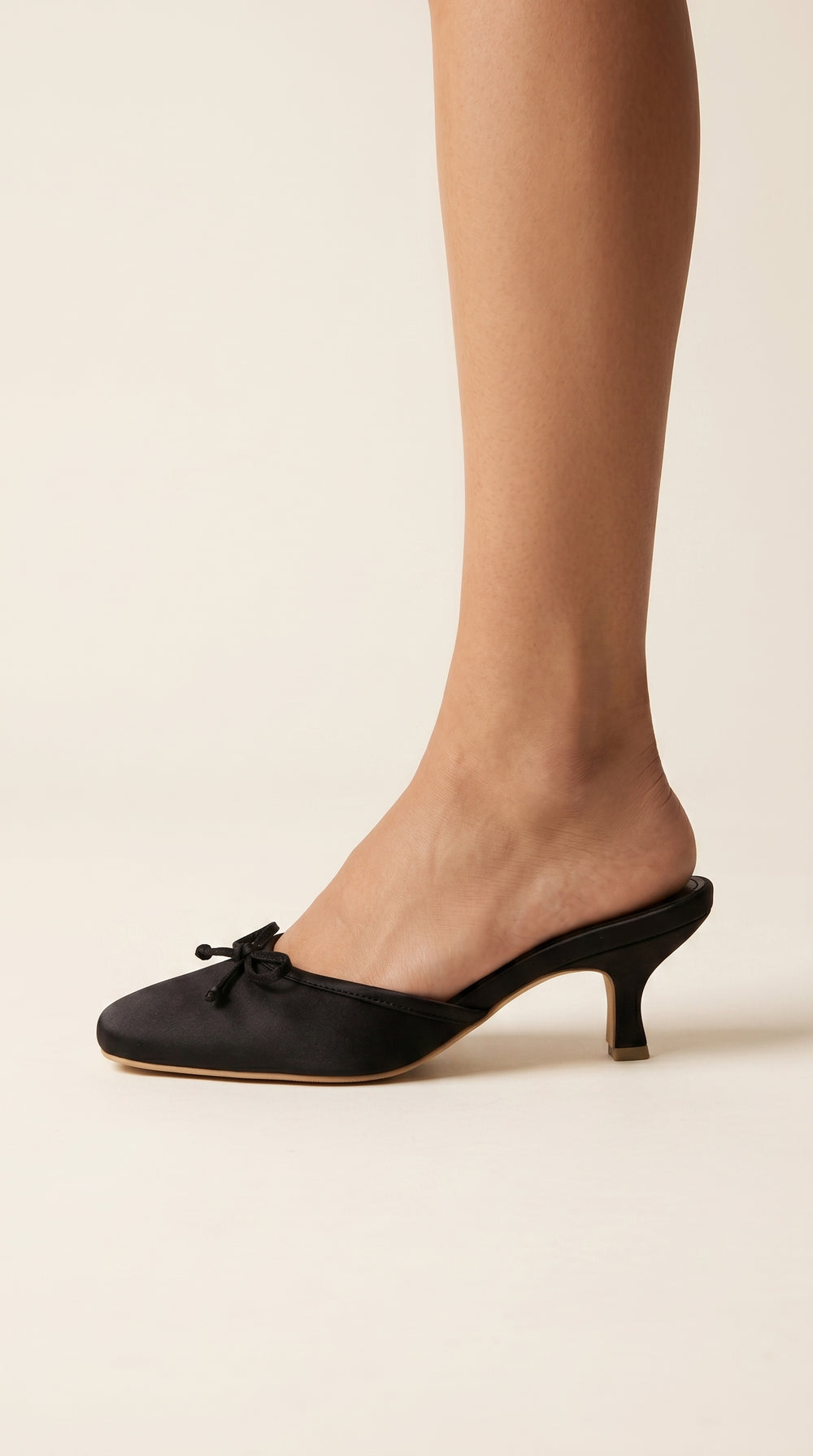 Black kitten heel shoes worn by a person on a beige background