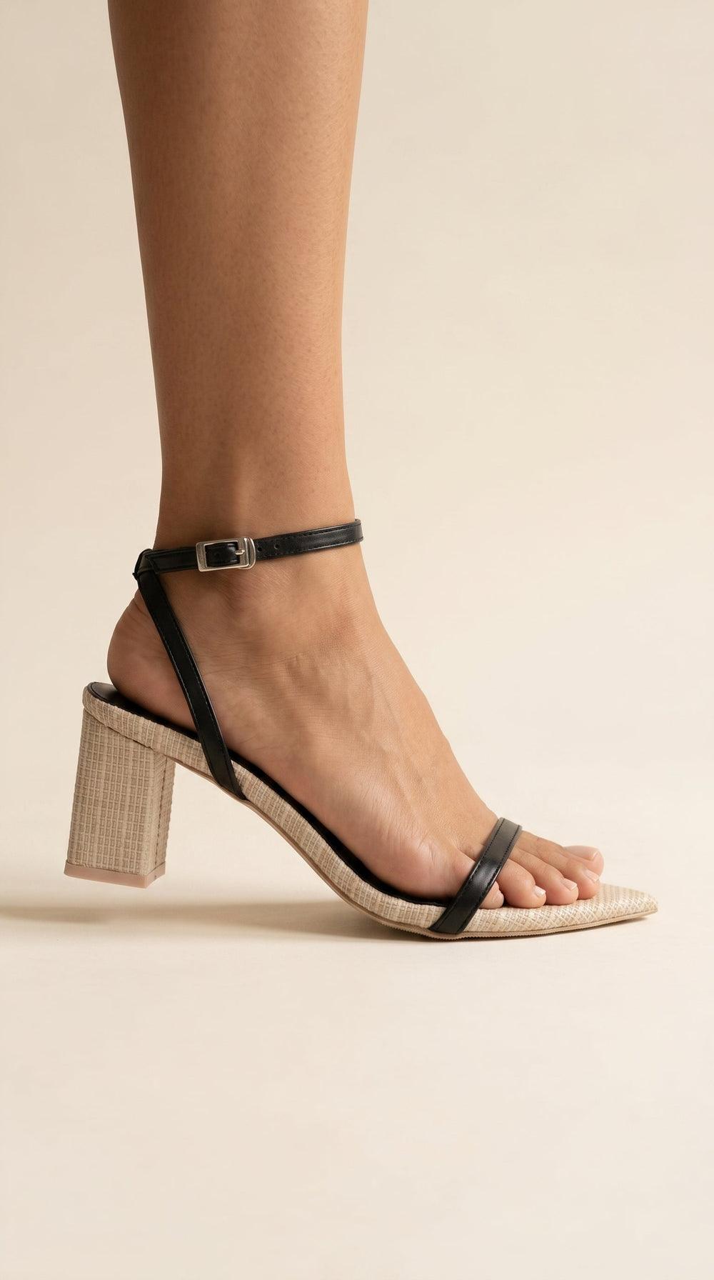 Black sandal with a block heel worn by a person on a beige background