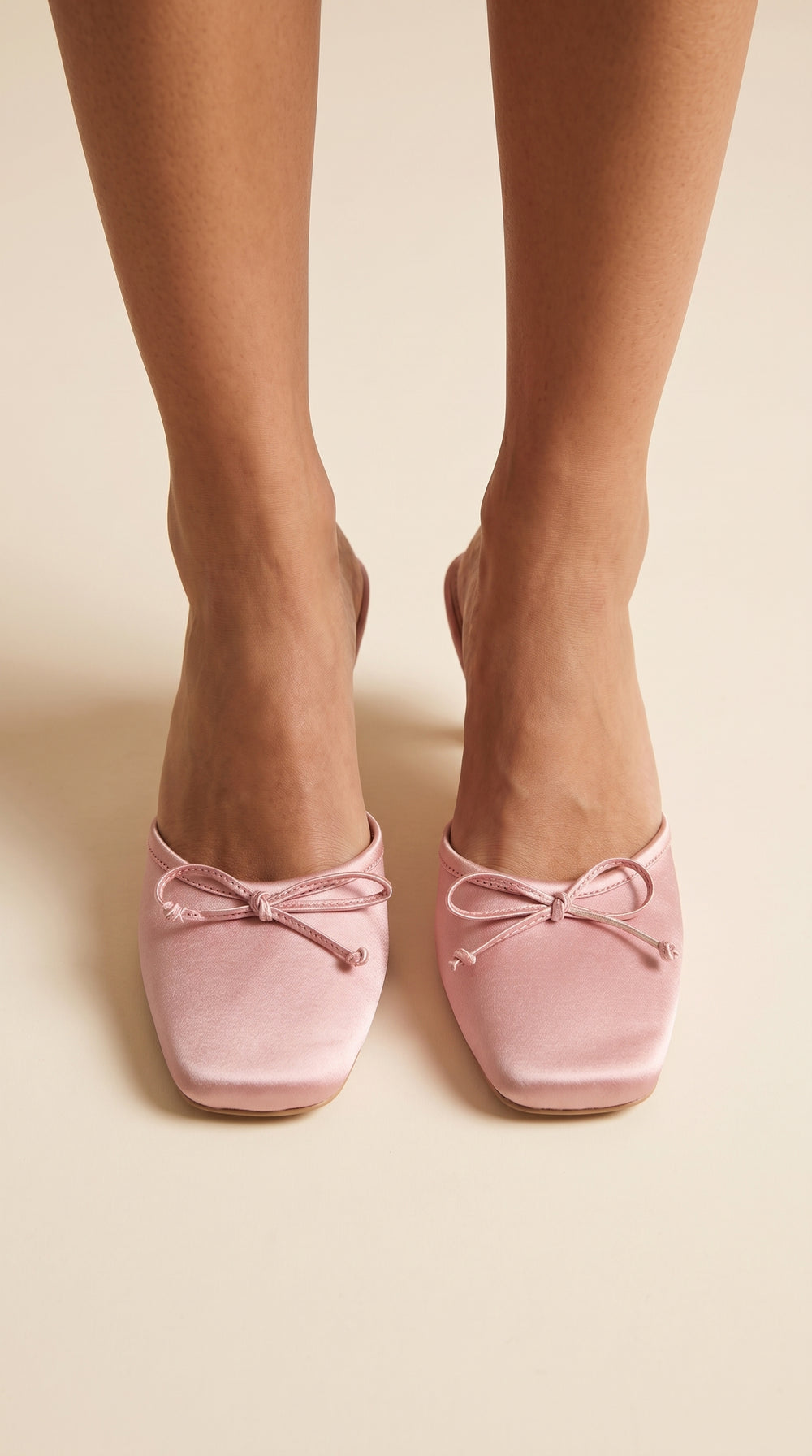 Pink ballet flats with bows worn by a person on a beige background