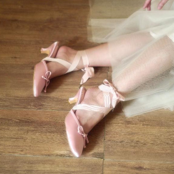 Pink high-heeled shoes with ribbons on a wooden floor