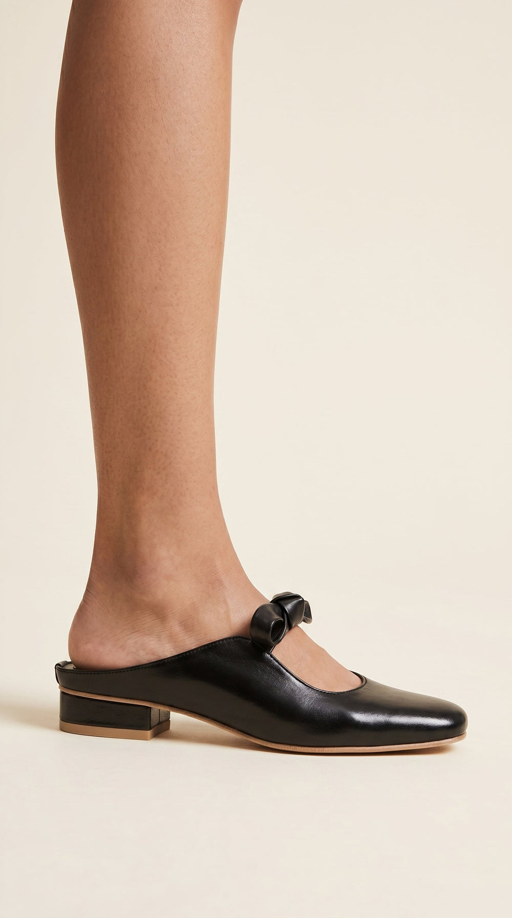 Black flat shoes with a bow detail worn by a person on a beige background