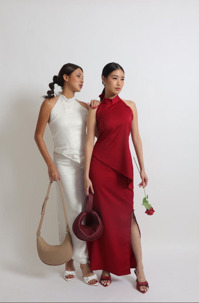 Two women, one in a white outfit and the other in a red dress, standing side by side against a plain background. maroon