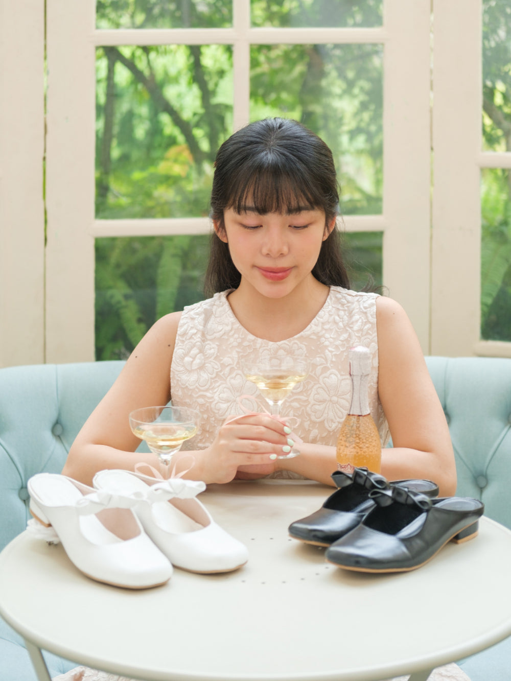 Woman sitting on a couch with white and black shoes and a glass of champagne.