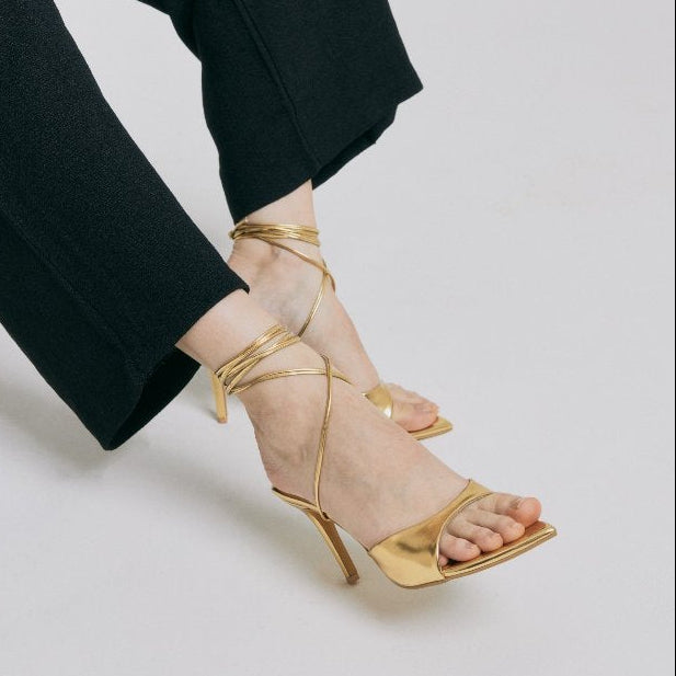 Gold (9 cm) high-heeled sandals worn with black pants on a light gray background