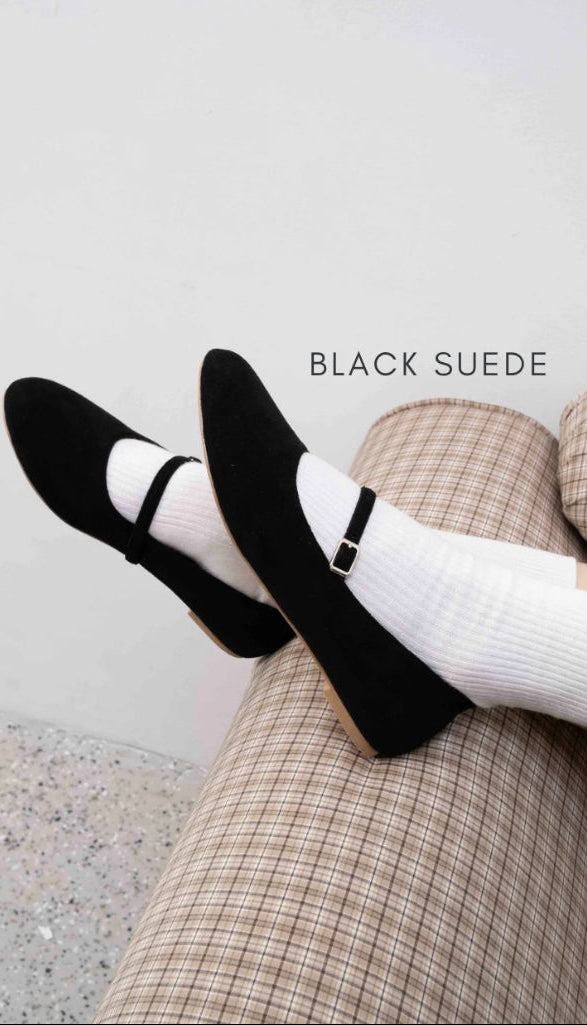 Black suede shoes worn with white socks and plaid pants on a light background
