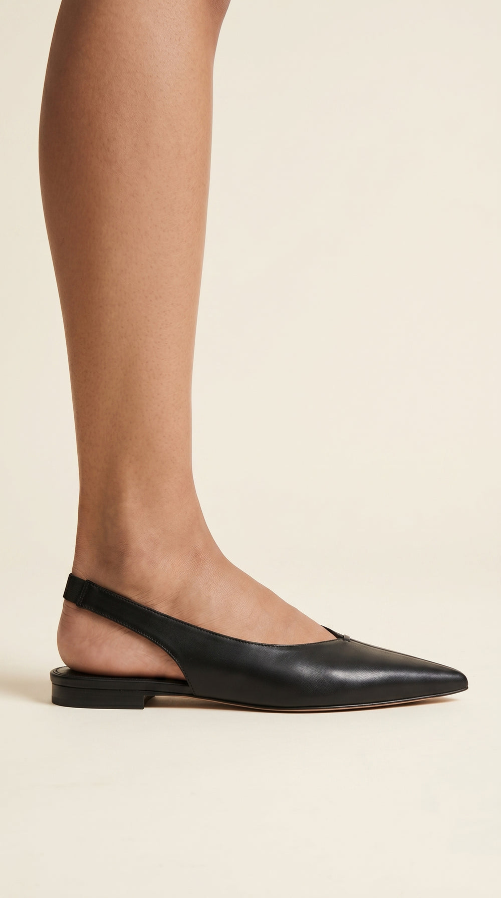 Black leather shoes worn with sheer tights on a beige background