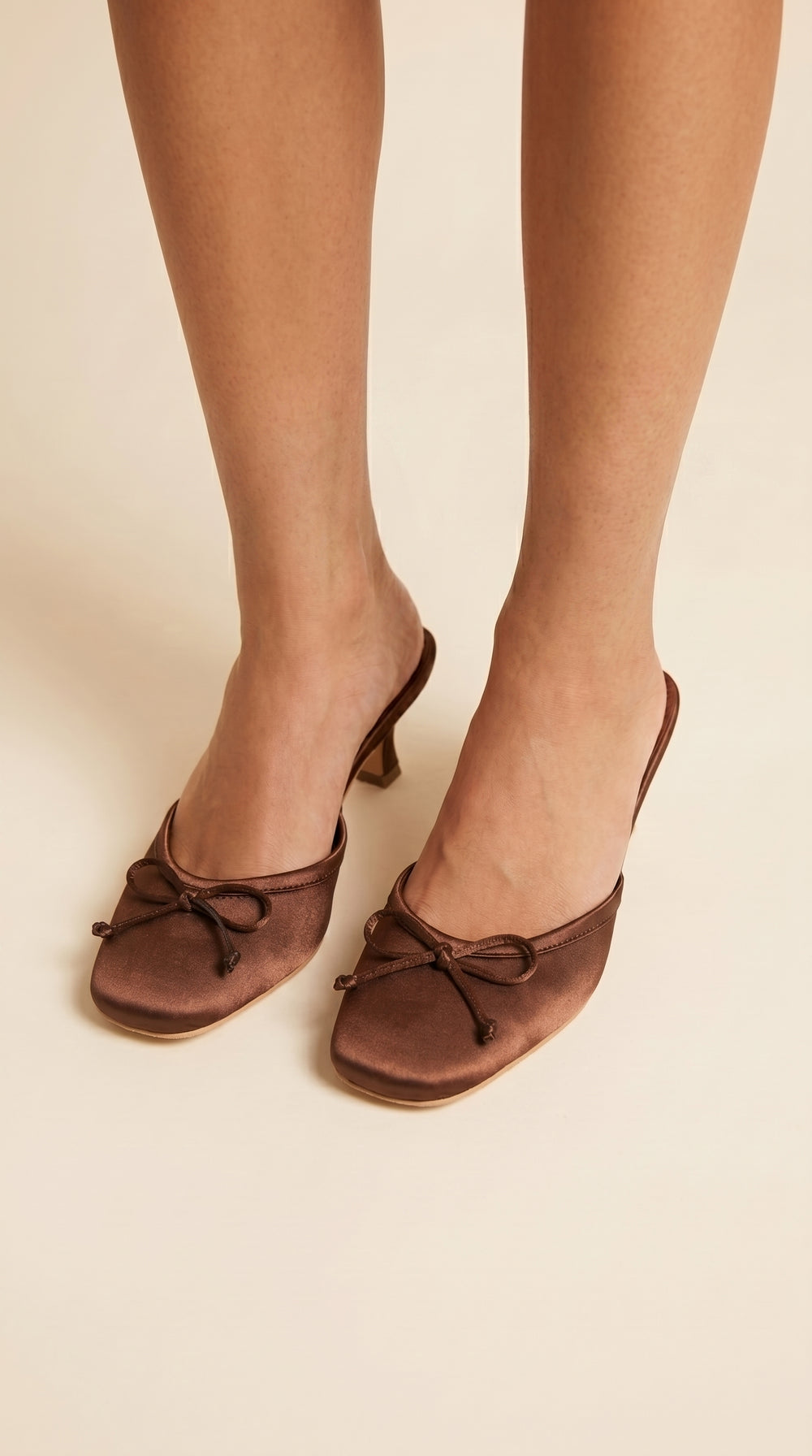 Brown shoes with bow details worn by a person on a beige background
