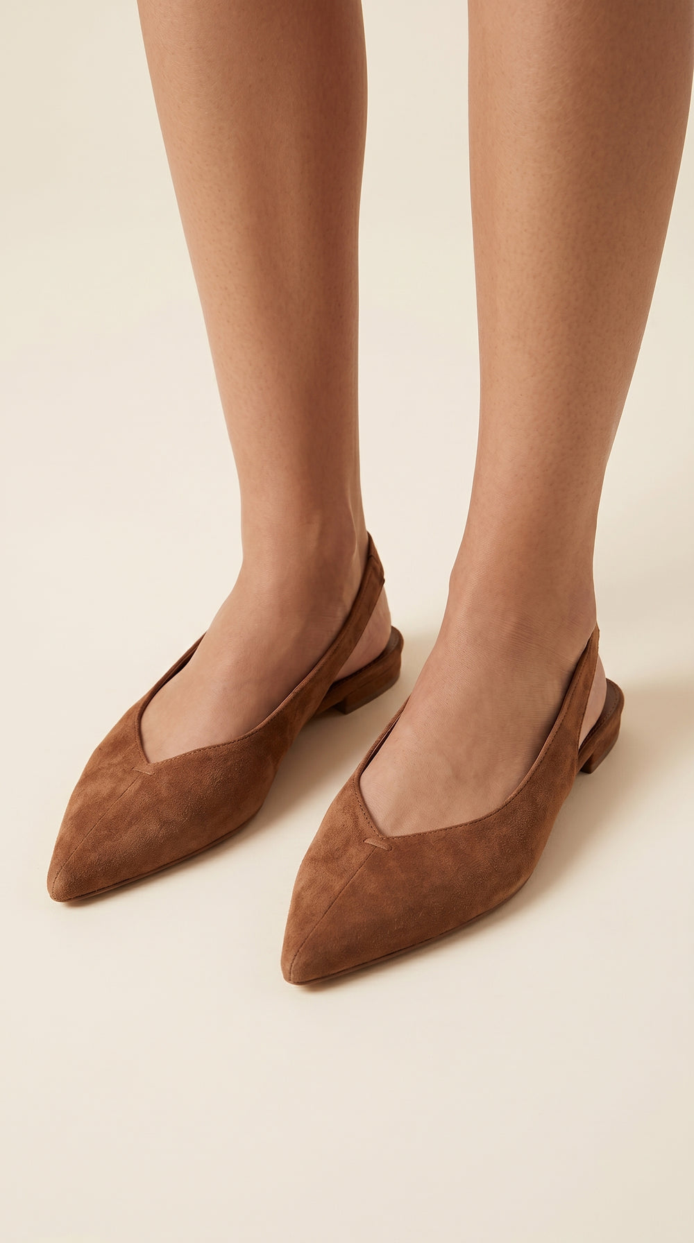 Brown suede shoes worn by a person on a beige background
