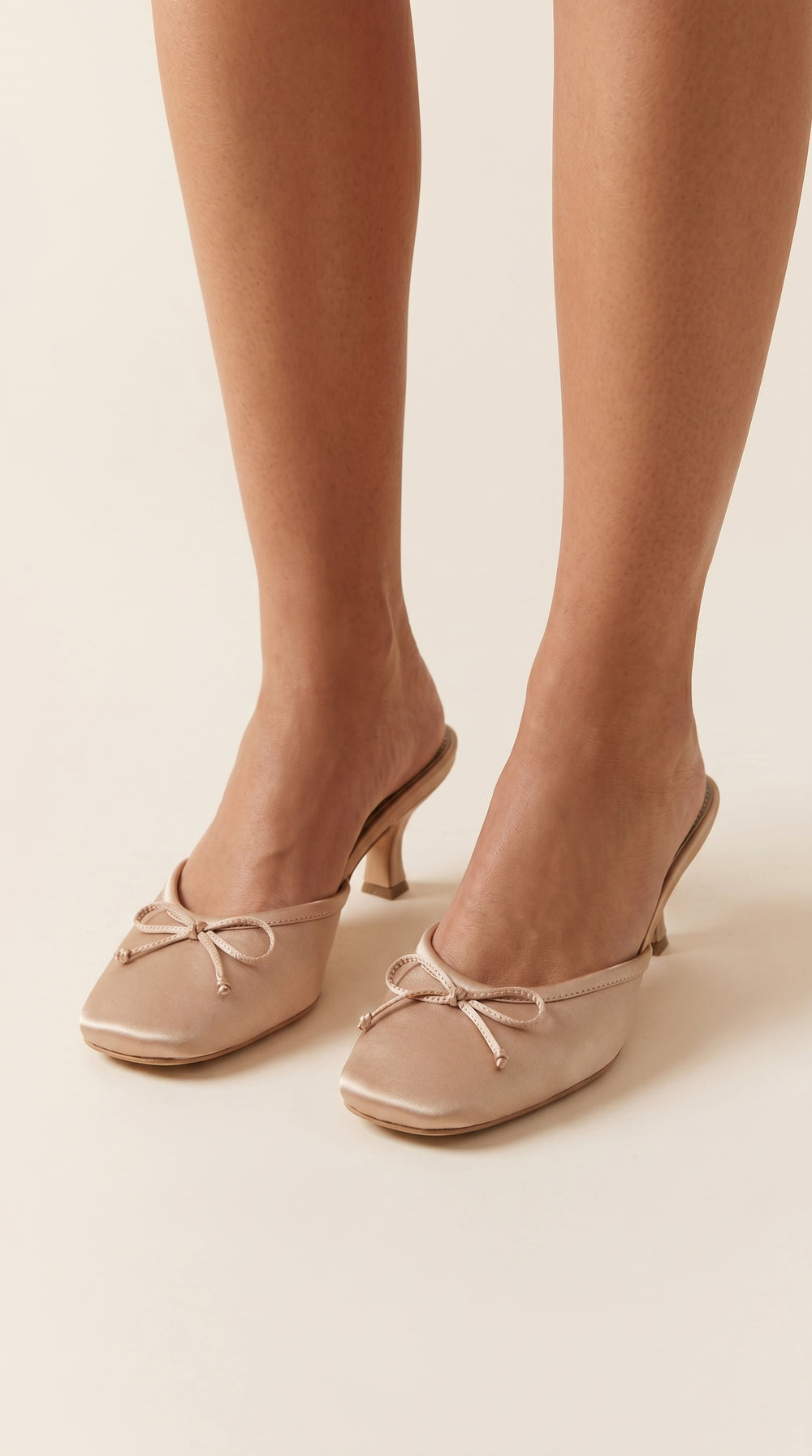 nude high-heeled shoes with bow details worn by a person on a beige background
