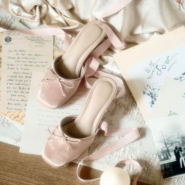 nude  heel shoes with ribbon on a textured surface with books and paper.