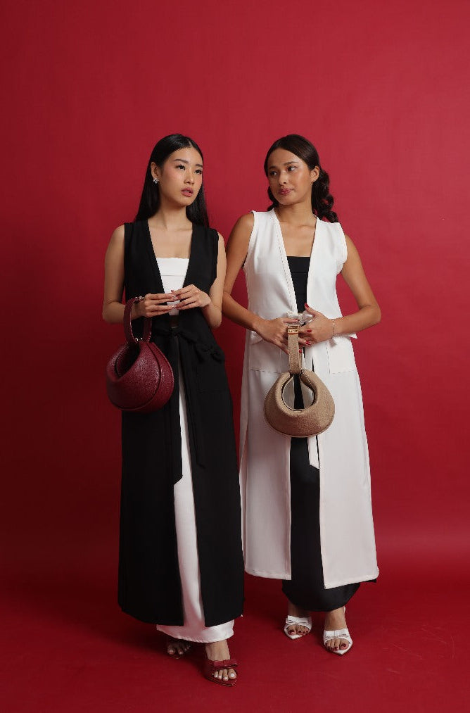 Two women holding handbags against a red background maroon white 