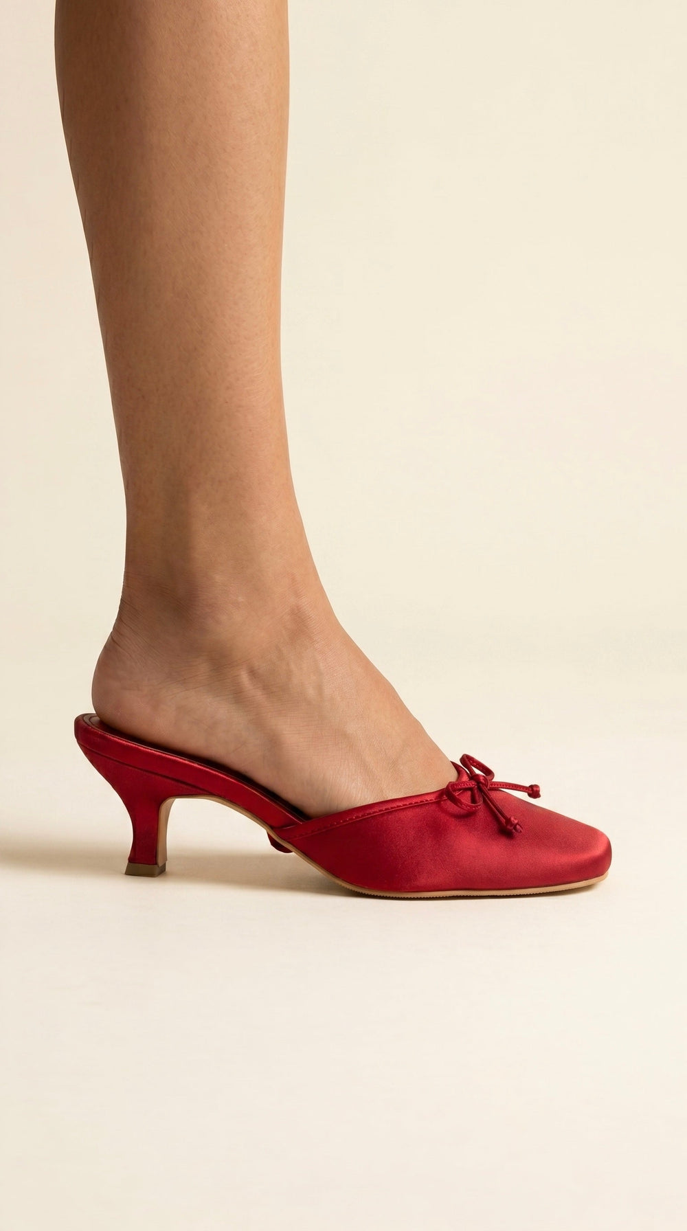 Red high-heeled shoes worn with beige tights on a neutral background