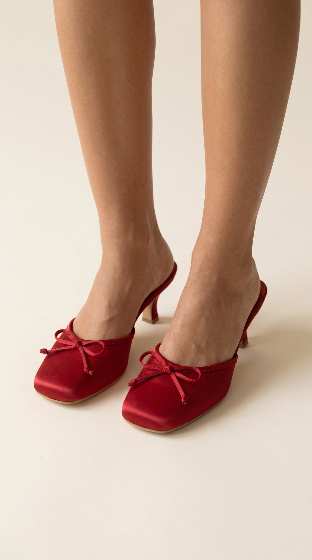 Red shoes with bow details worn by a person on a plain background