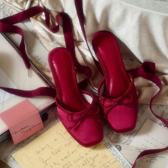 Red high-heeled shoes with ribbons on a textured surface